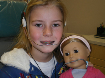 A young girl with braces holding an American Girl doll with braces.